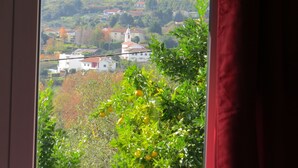 Une vue d’une ville avec ses bâtiments et son église, aperçue à travers une fenêtre ornée d’un rideau rouge.