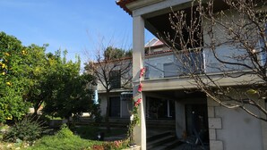 Un immeuble résidentiel doté d’un balcon, d’un jardin avec différentes plantes et fleurs, et d’un ciel bleu dégagé.