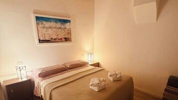 A bedroom with a wooden ceiling, a bed with a striped blanket, a bedside table with a lamp, and a painting on the wall.