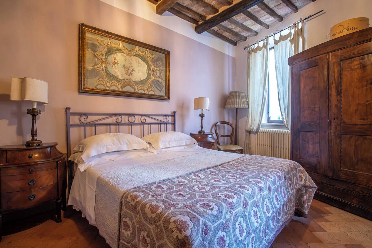 Un dormitorio con una cama grande, mesitas de noche de madera, un aparador, un espejo amplio y un armario.