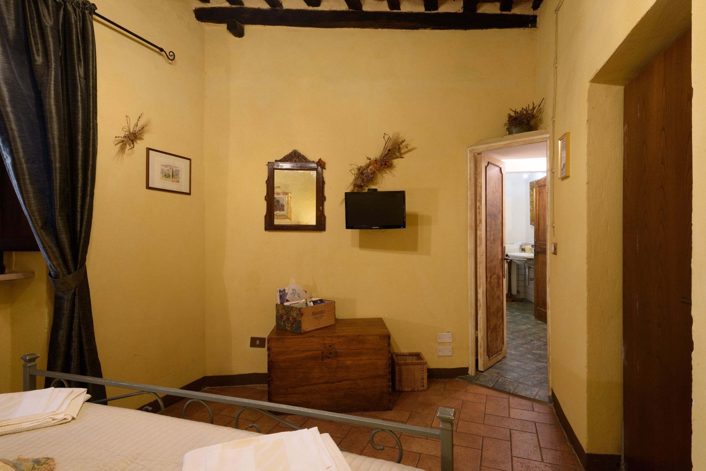 Ein Schlafzimmer mit einem Bett, einer Holzkiste, einem Spiegel und einem Fernseher an der Wand.