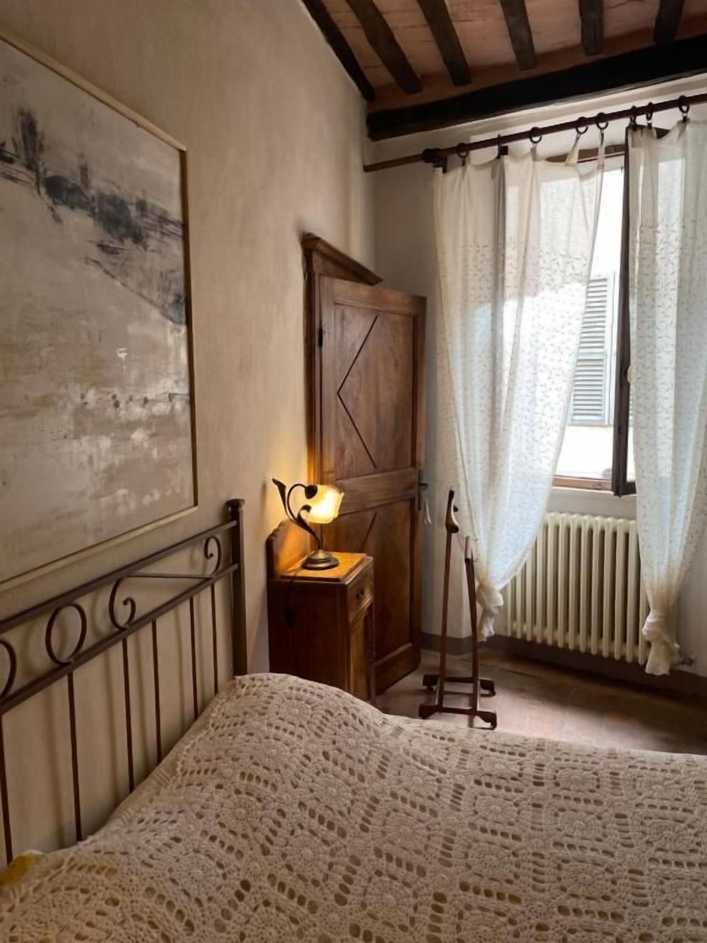 Ein Schlafzimmer mit einem Holzbett, einem Nachttisch mit Lampe, einem Heizkörper und einem Fenster mit Vorhängen.