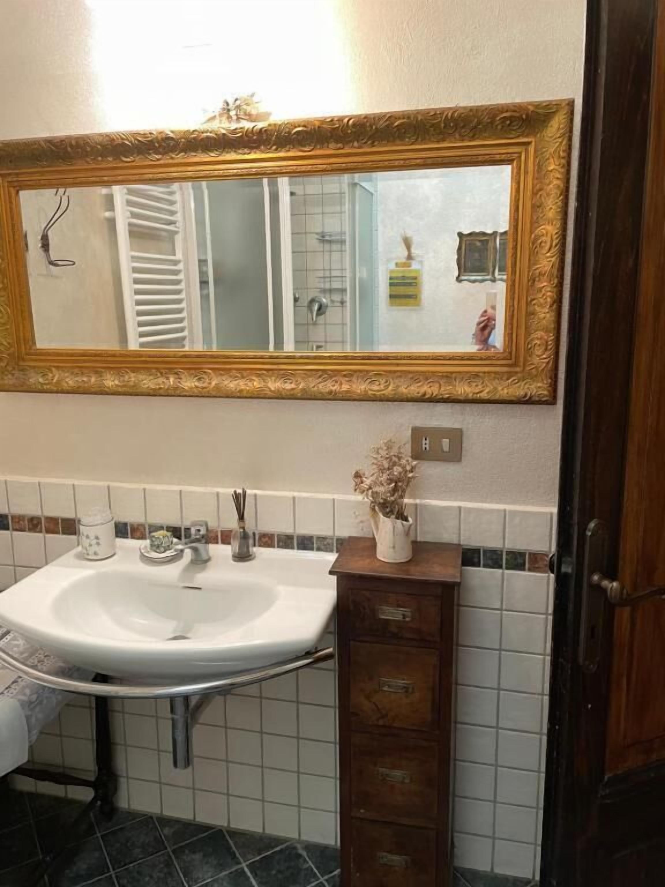Un baño con un lavabo blanco, un espejo con un marco dorado ornamentado y un mueble de madera debajo.