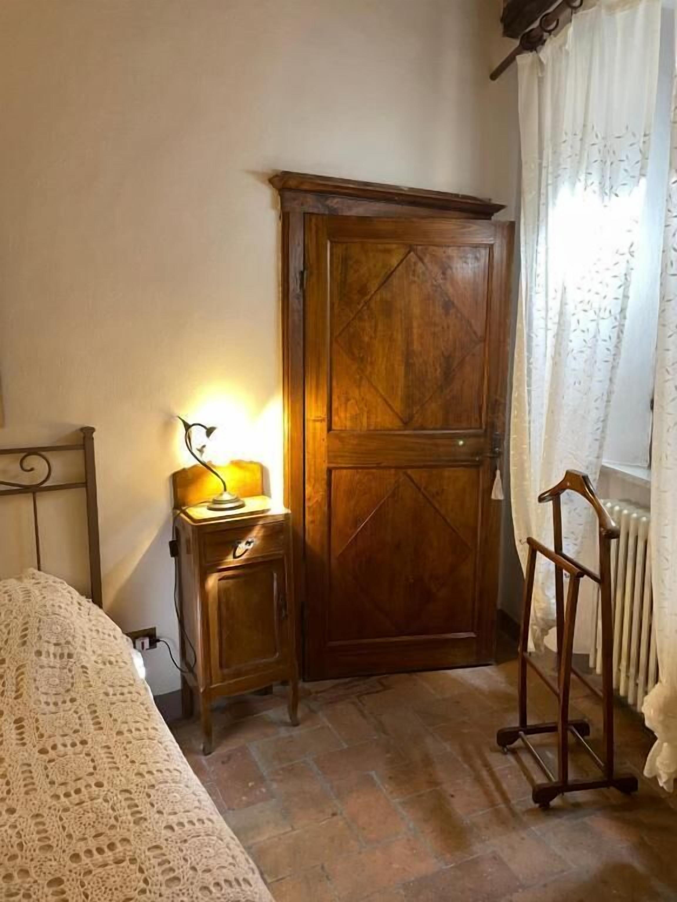 Ein Schlafzimmer mit einem Holzkleiderschrank, einem Nachttisch mit Lampe, einer Heizung und einem Sessel.