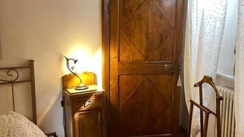 Ein Schlafzimmer mit einem Holzkleiderschrank, einem Nachttisch mit Lampe, einer Heizung und einem Sessel.