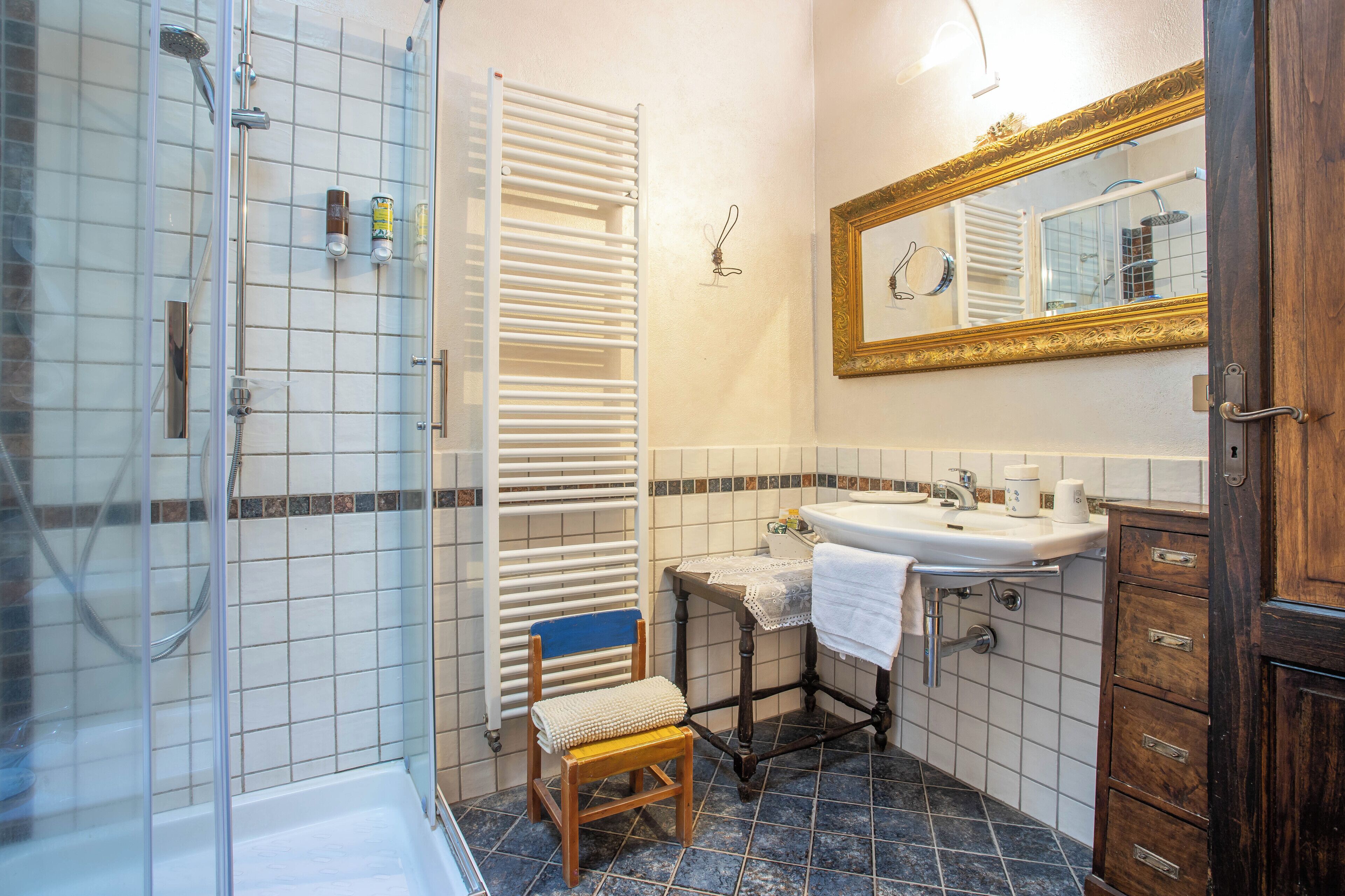 Ein Badezimmer mit Dusche, Waschbecken, Spiegel und einem Holzstuhl.