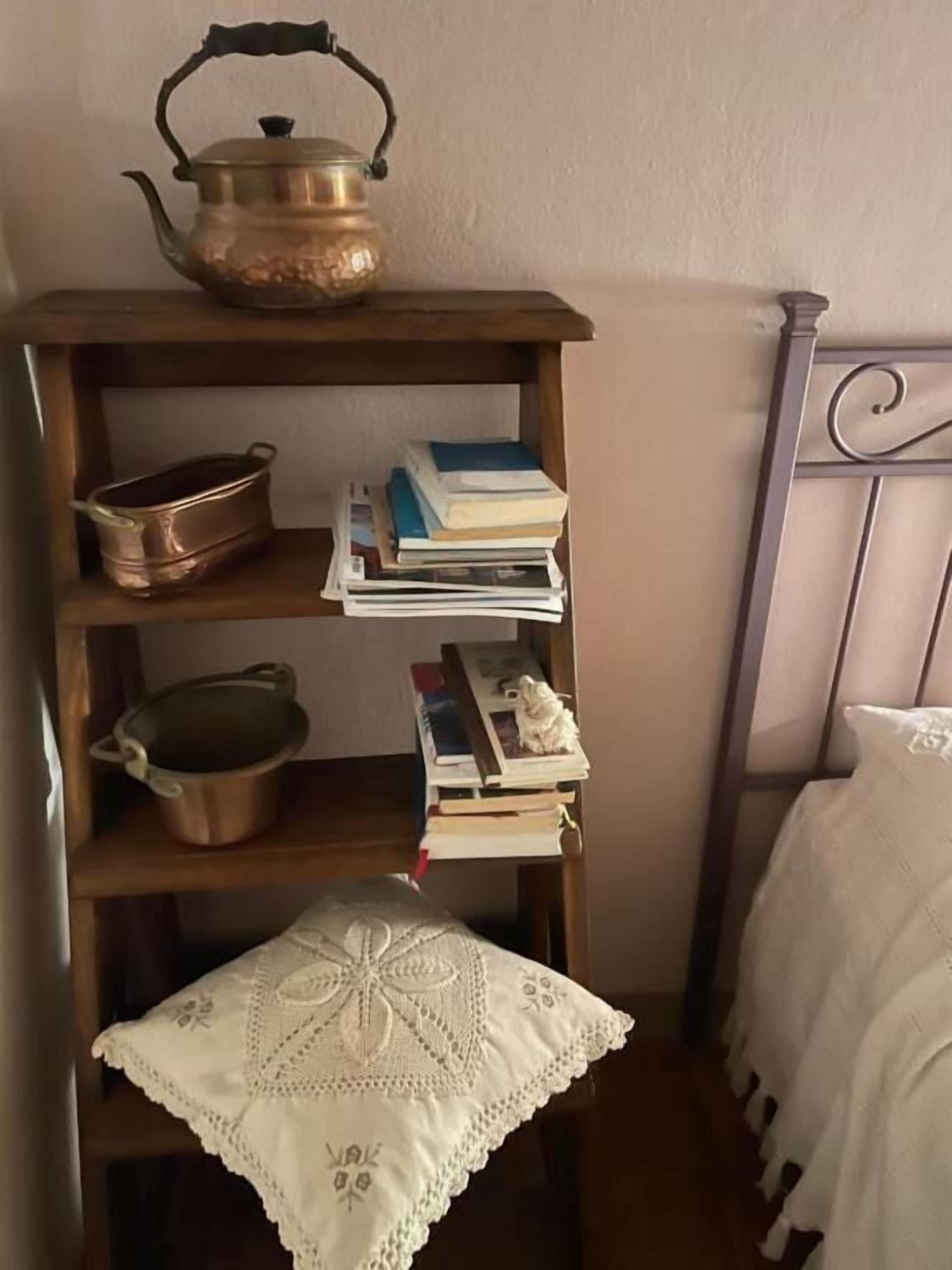 A wooden shelf with a brass kettle, copper pot, and books.