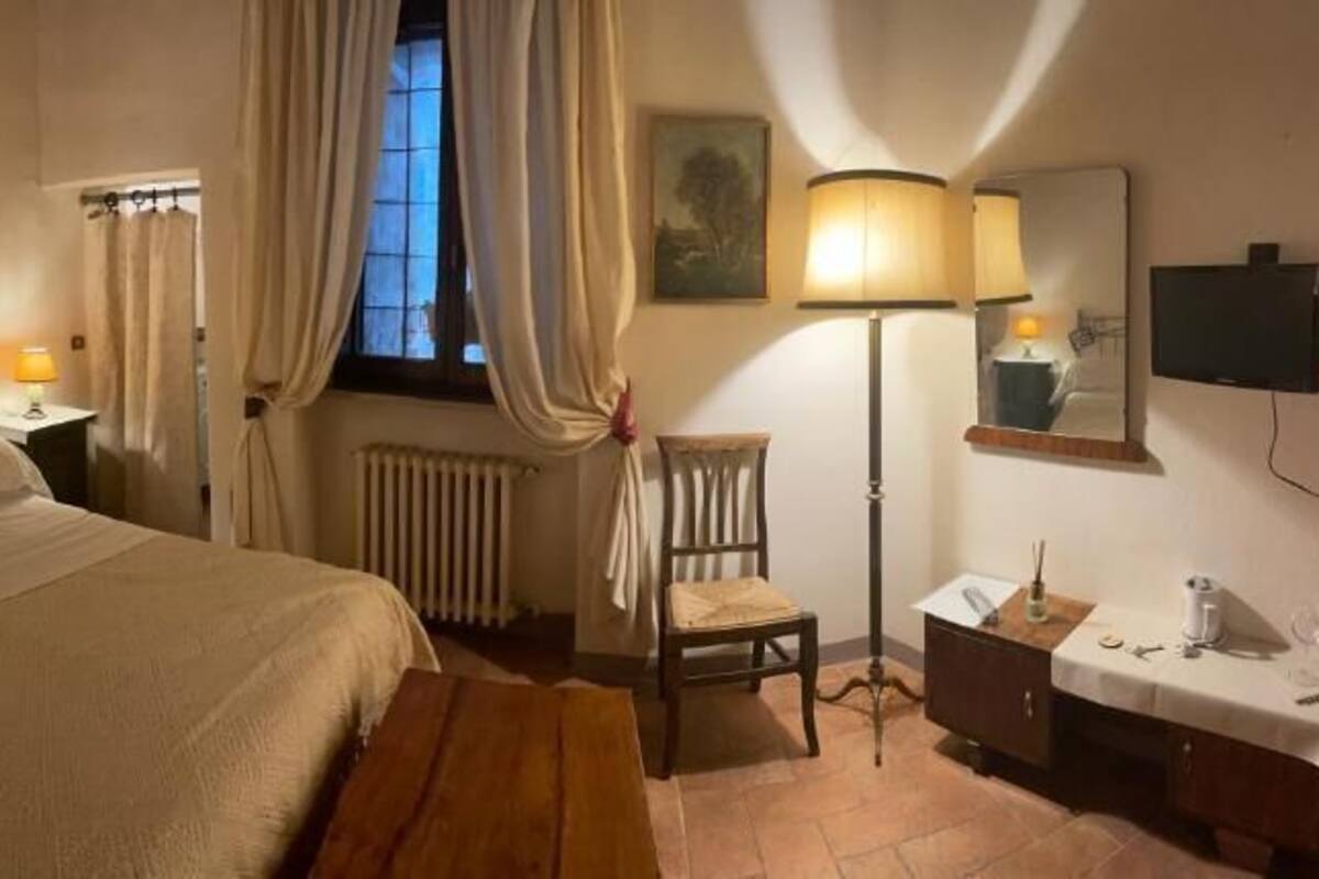 Un dormitorio con cama, mesitas de noche, una silla, un escritorio, una lámpara, un radiador y una televisión.