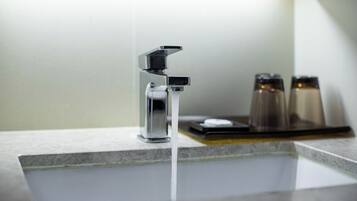 Un baño moderno con un grifo cromado, un recipiente de vidrio y un salero sobre la encimera.