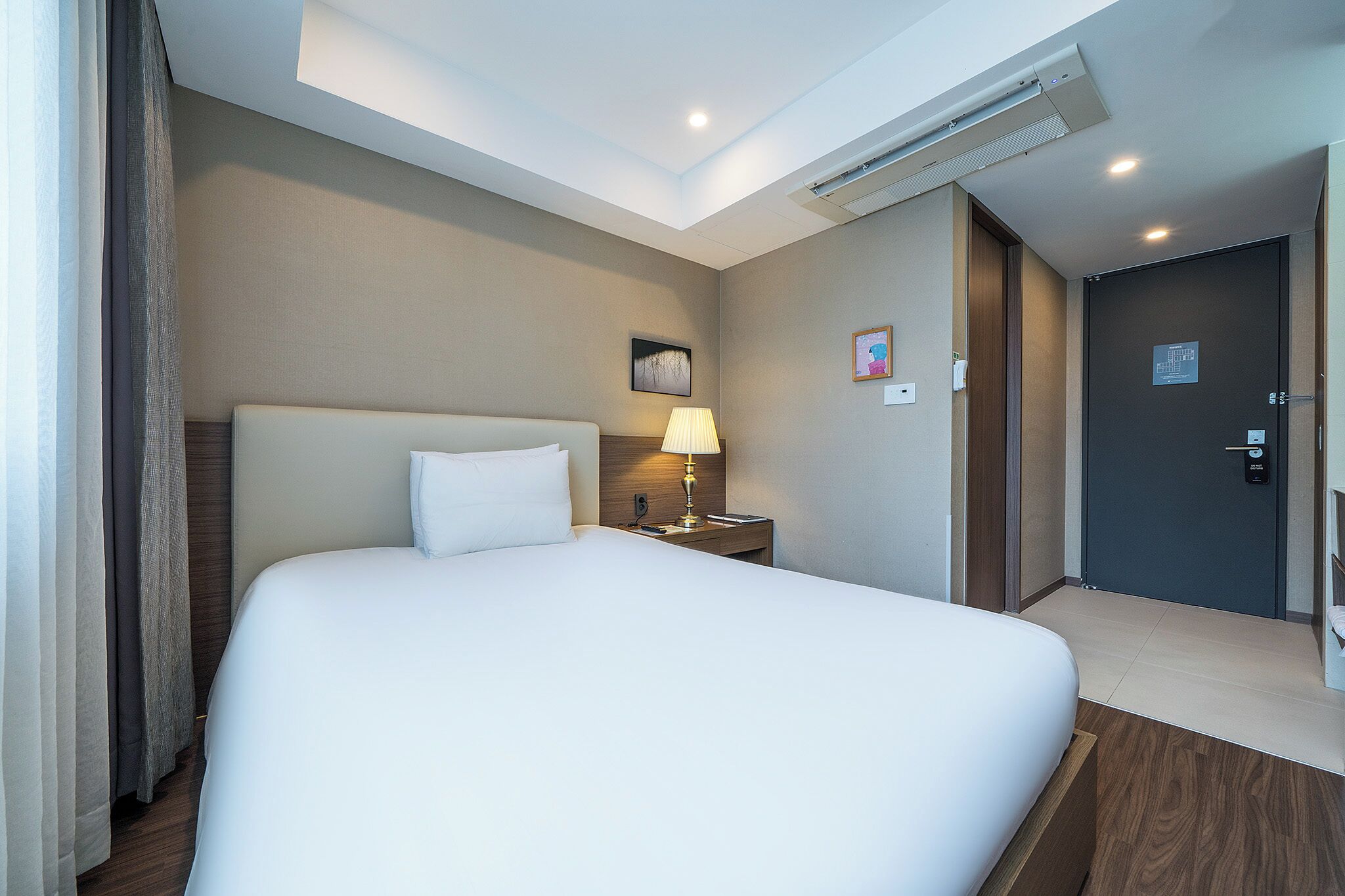 Une chambre d’hôtel avec un grand lit, une lampe de chevet, une œuvre d’art accrochée au mur et une porte avec une pancarte.