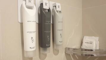 A bathroom with a wall-mounted dispenser for body lotion, shampoo, conditioner, and body wash. A shower towel is visible on a rack.