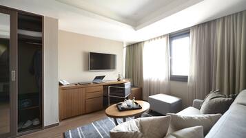 Ett modernt hotellrum med ett skrivbord i trä, en platt-TV, en soffa och ett stort fönster med gardiner.