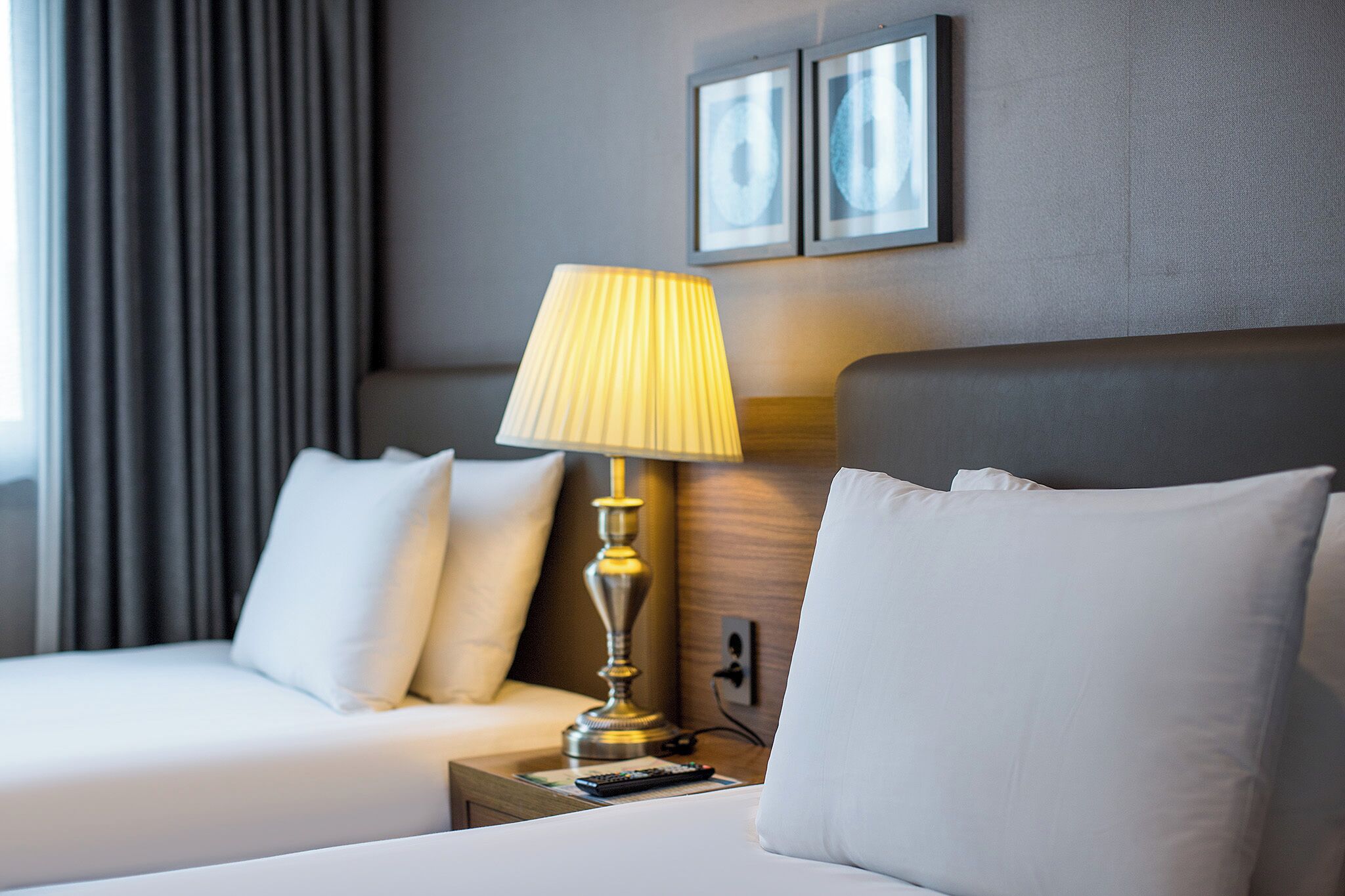 A hotel room with a bed, a bedside lamp, a remote control, and two framed pictures on the wall.