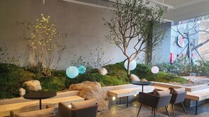 A modern outdoor seating area with wicker chairs and benches, surrounded by a landscaped garden with rocks and plants. - Busan Business Hotel (Busan)