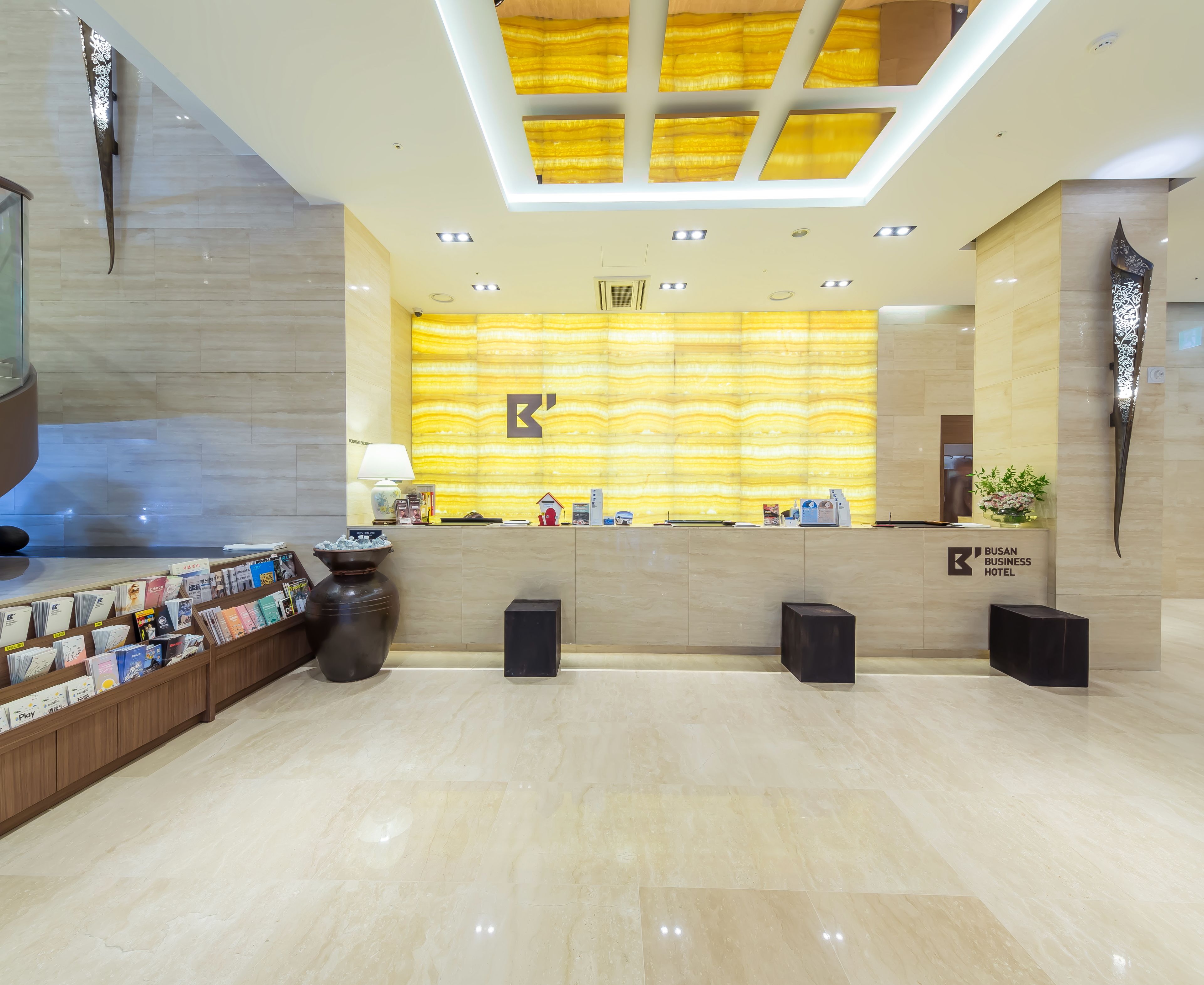 En hotellobby med modern design, med en receptionsdisk, en stor vas med blommor och ett ställ med broschyrer.