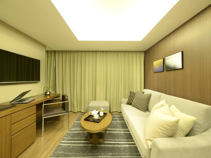 Una habitación de hotel moderna con televisión de pantalla plana, un escritorio con una computadora portátil, un sofá y una mesa de centro con una bandeja.