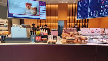 A bakery counter with pastries and beverages, a digital menu, and staff behind the counter.