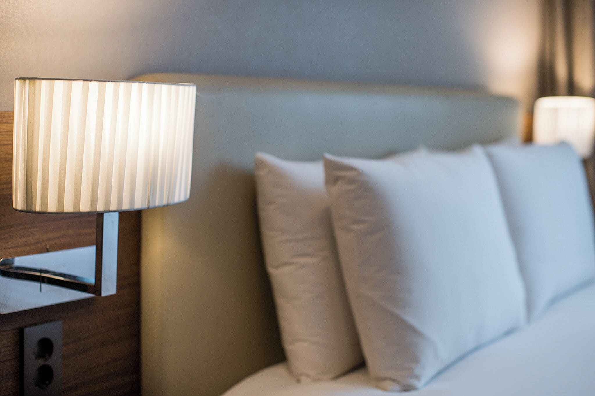 Un lit bien fait, avec une literie et des oreillers blancs, une table de chevet avec une lampe et une tête de lit.