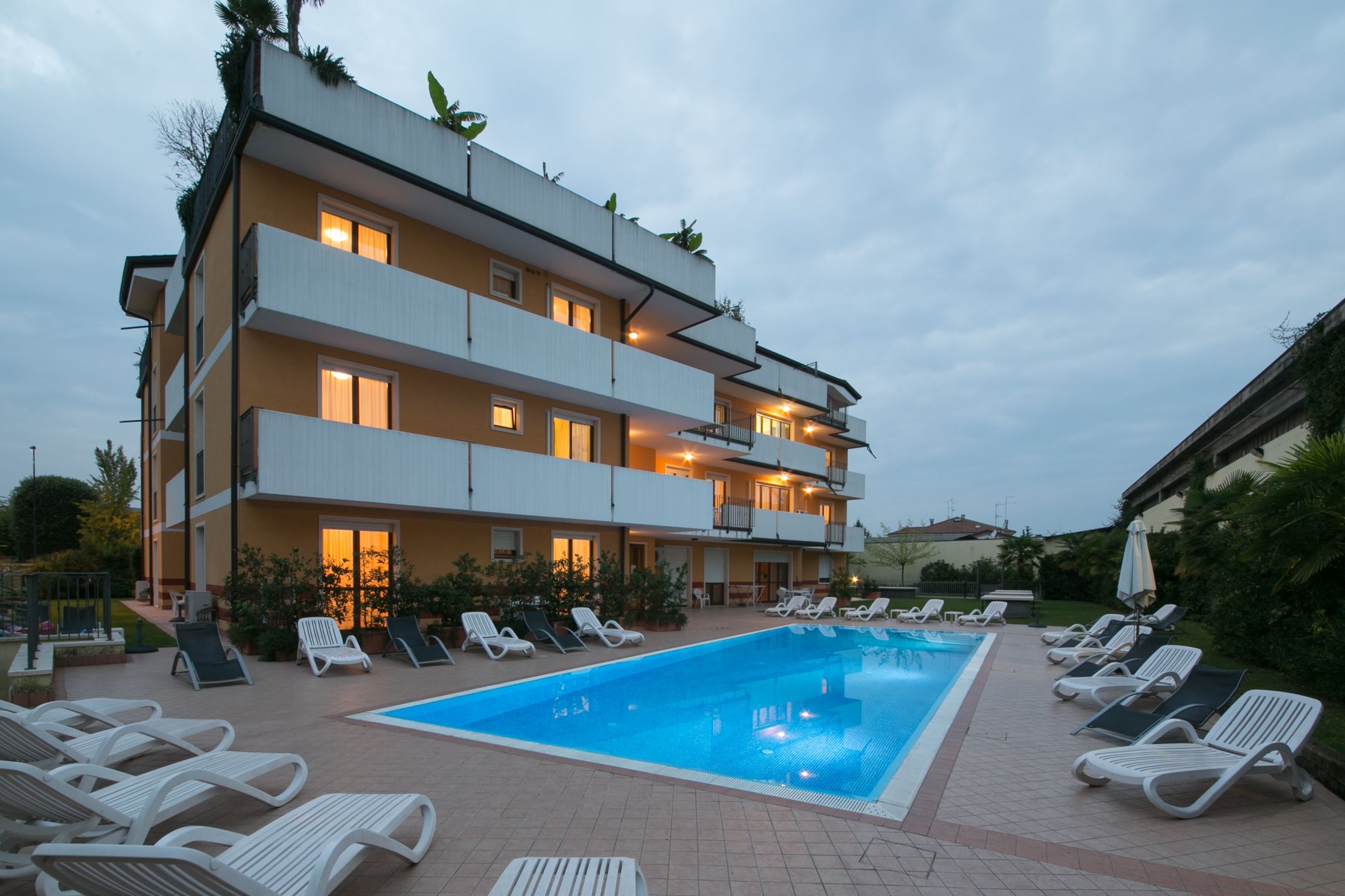 A multi-story hotel with a swimming pool, sun loungers, and a garden area.