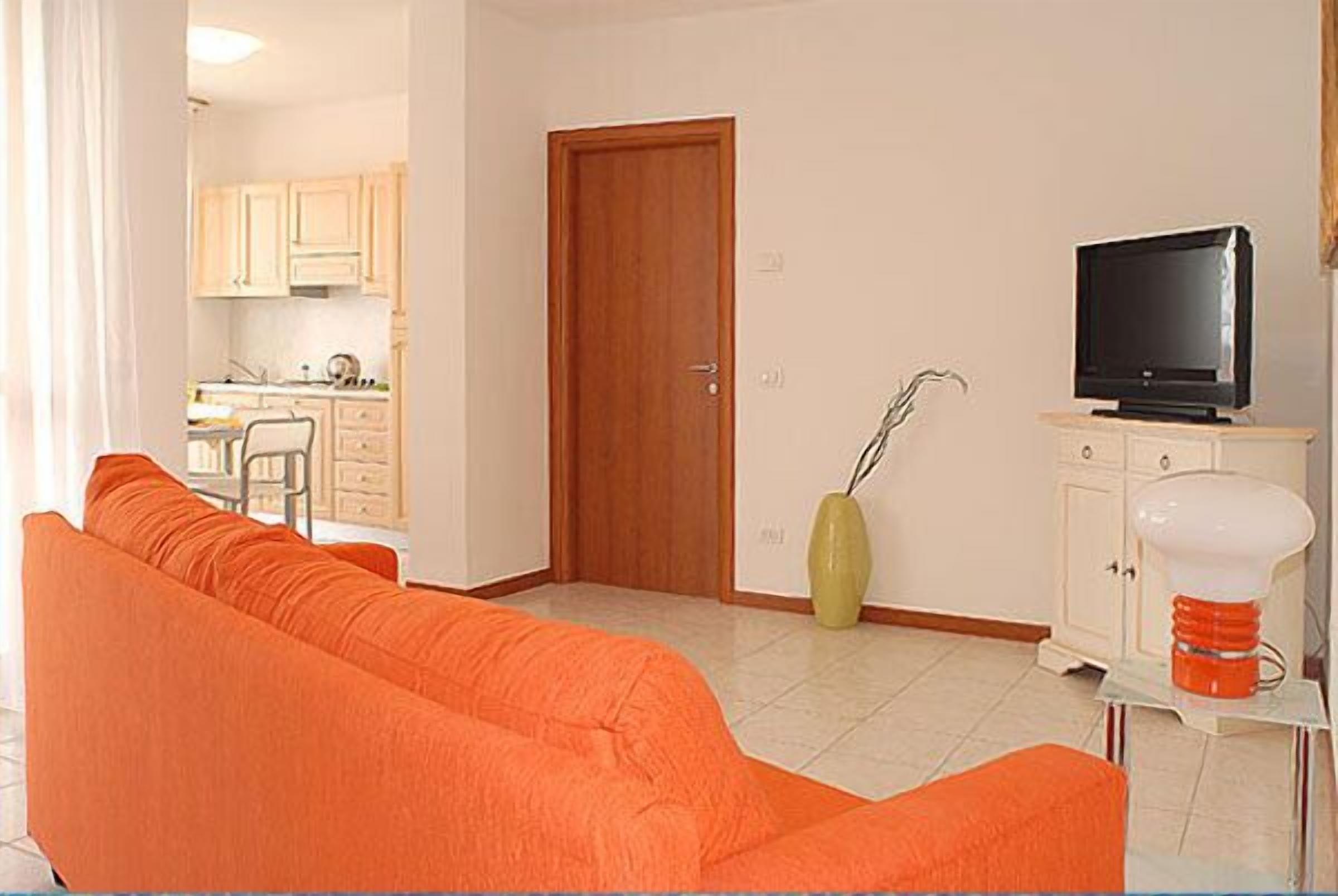 Een woonkamer met een bank, een televisie, een kast en een deur naar een keuken.