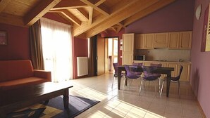 A spacious living area with a wooden ceiling, a sofa, a dining table with chairs, and a kitchen in the background. - Residence Garda Palace  (Peschiera del Garda)