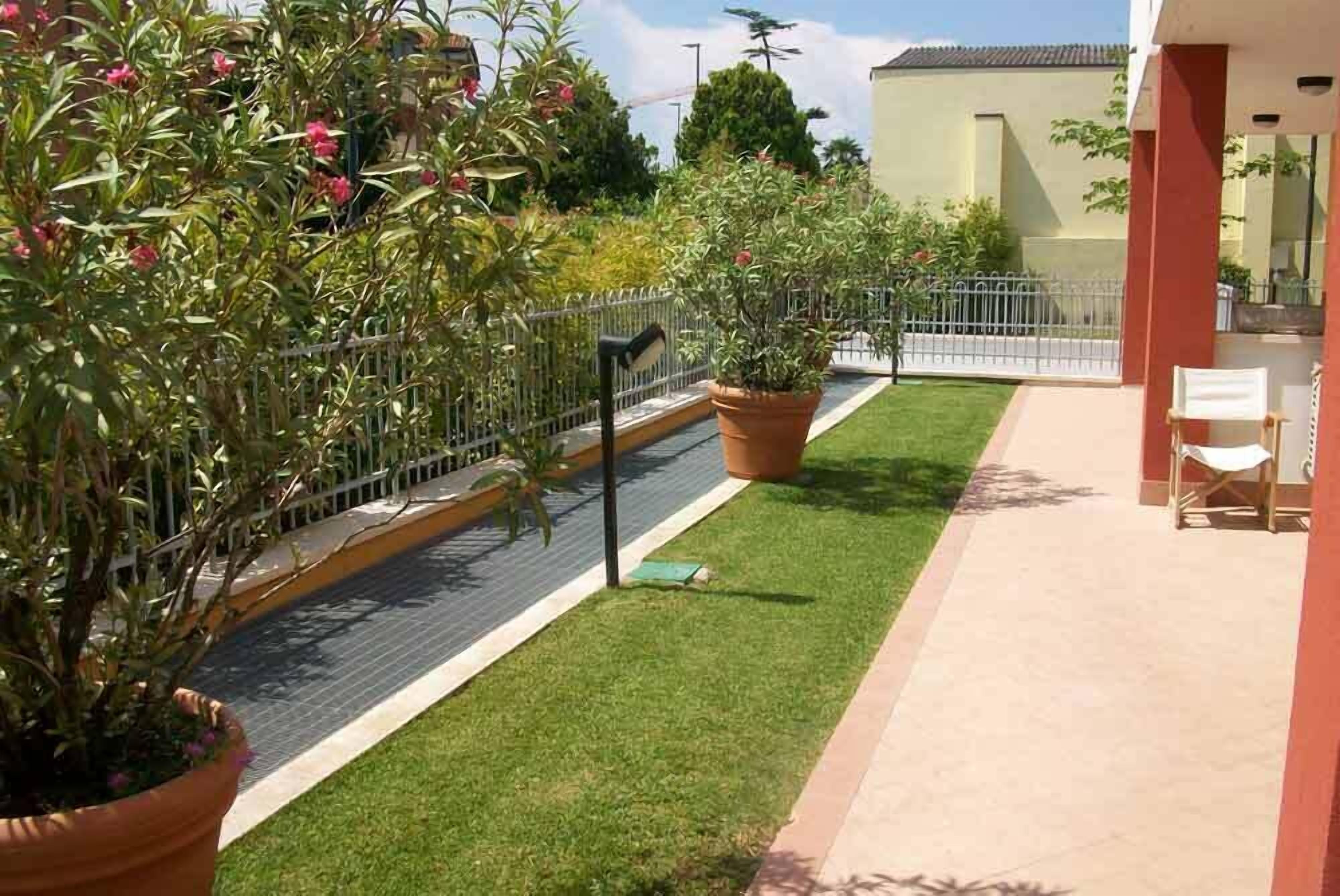 Un balcón con un pequeño césped, plantas en macetas y una silla.