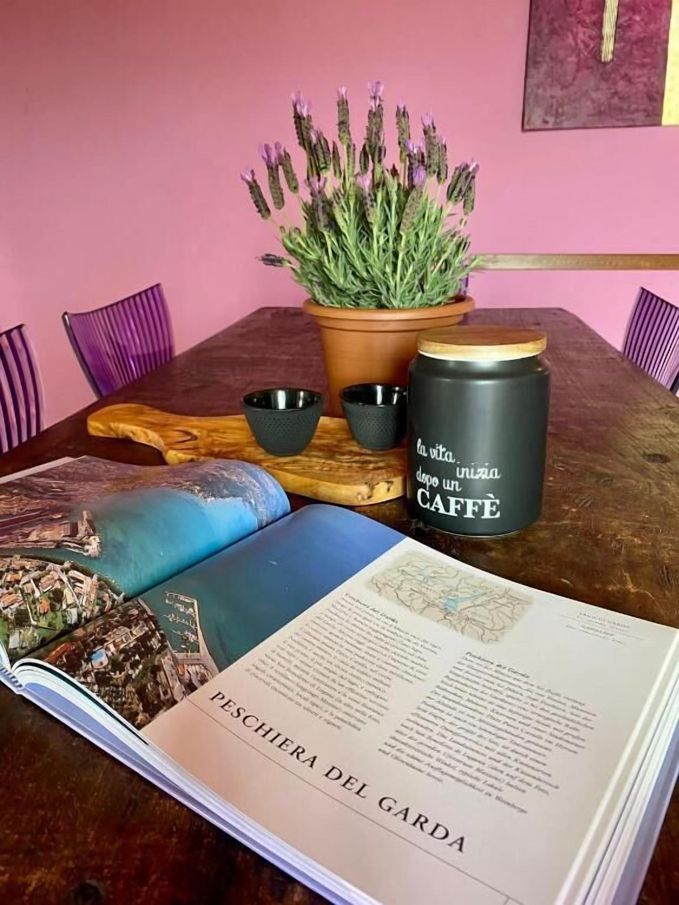 Ein Tisch mit einem Buch mit dem Titel 'Peschiera del Garda', einer Topfpflanze, zwei schwarzen Tassen und einem Behälter mit Schrift.
