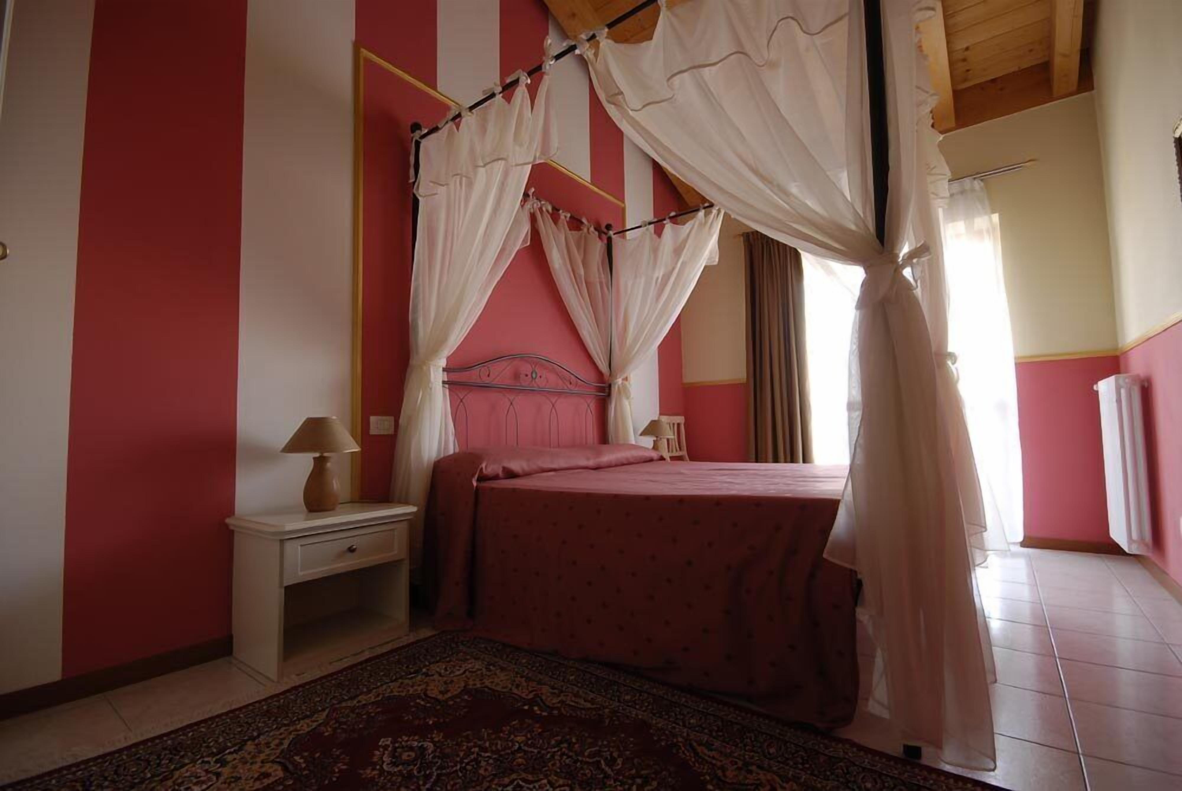 A bedroom with a four-poster bed, a nightstand, a lamp, and a patterned rug.