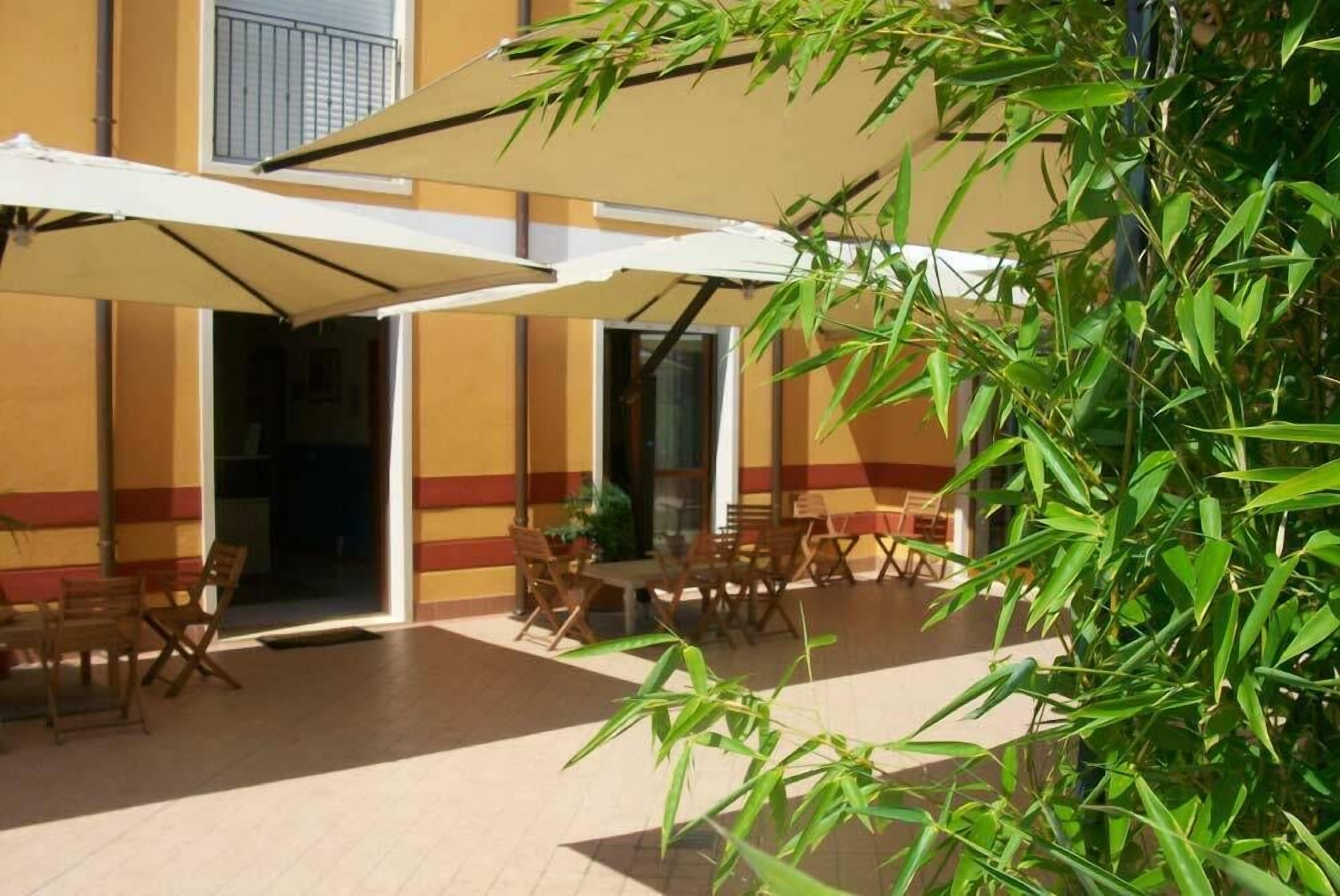 Eine Außenpatio-Terrasse mit Tischen und Stühlen, einem großen Sonnenschirm und einem Gebäude mit gelb-roten Wänden.