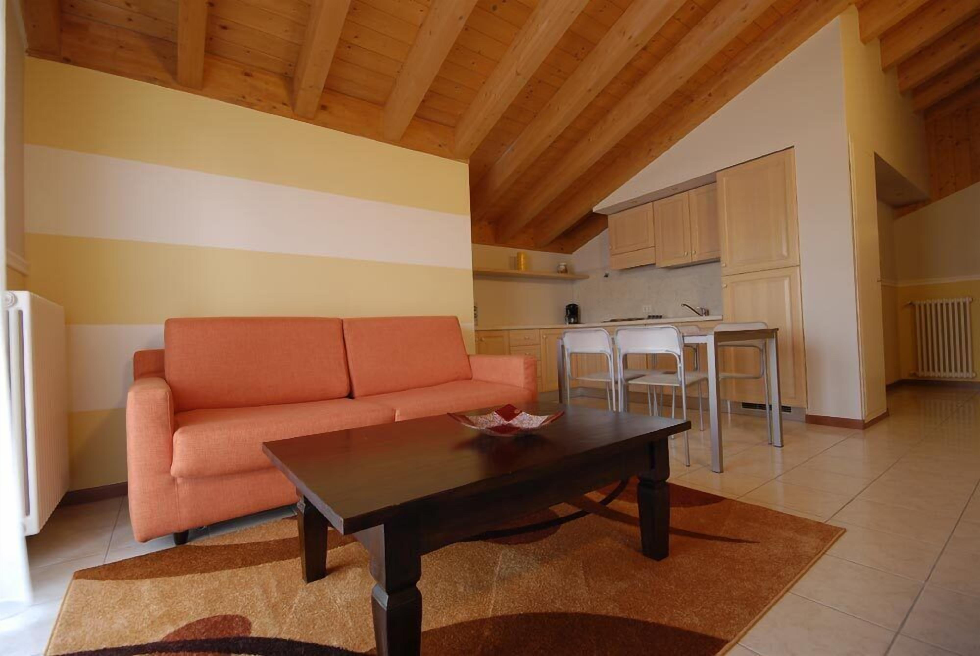 A cozy living area with a sofa and a coffee table, a kitchen with cabinets and a dining table, and a wooden ceiling.
