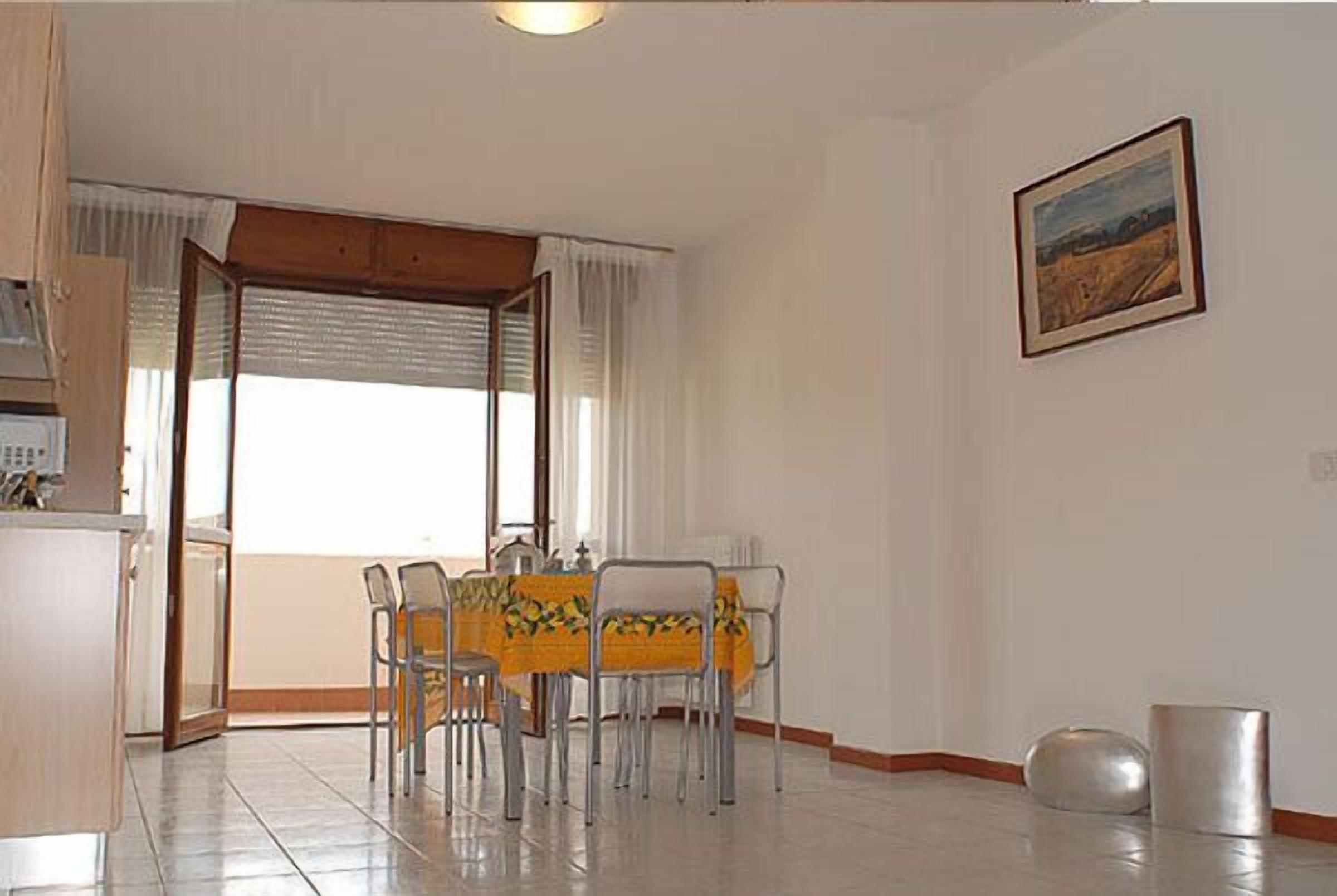 A dining area with a table set for four, a window with curtains, and a painting on the wall.