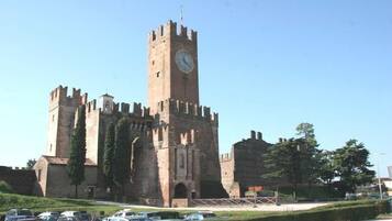 A historic castle with a prominent clock tower, surrounded by a parking lot and greenery.