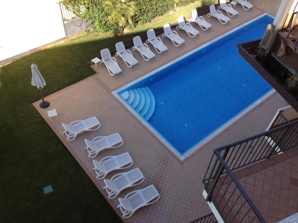A swimming pool with lounge chairs and a small table, surrounded by a tiled deck.