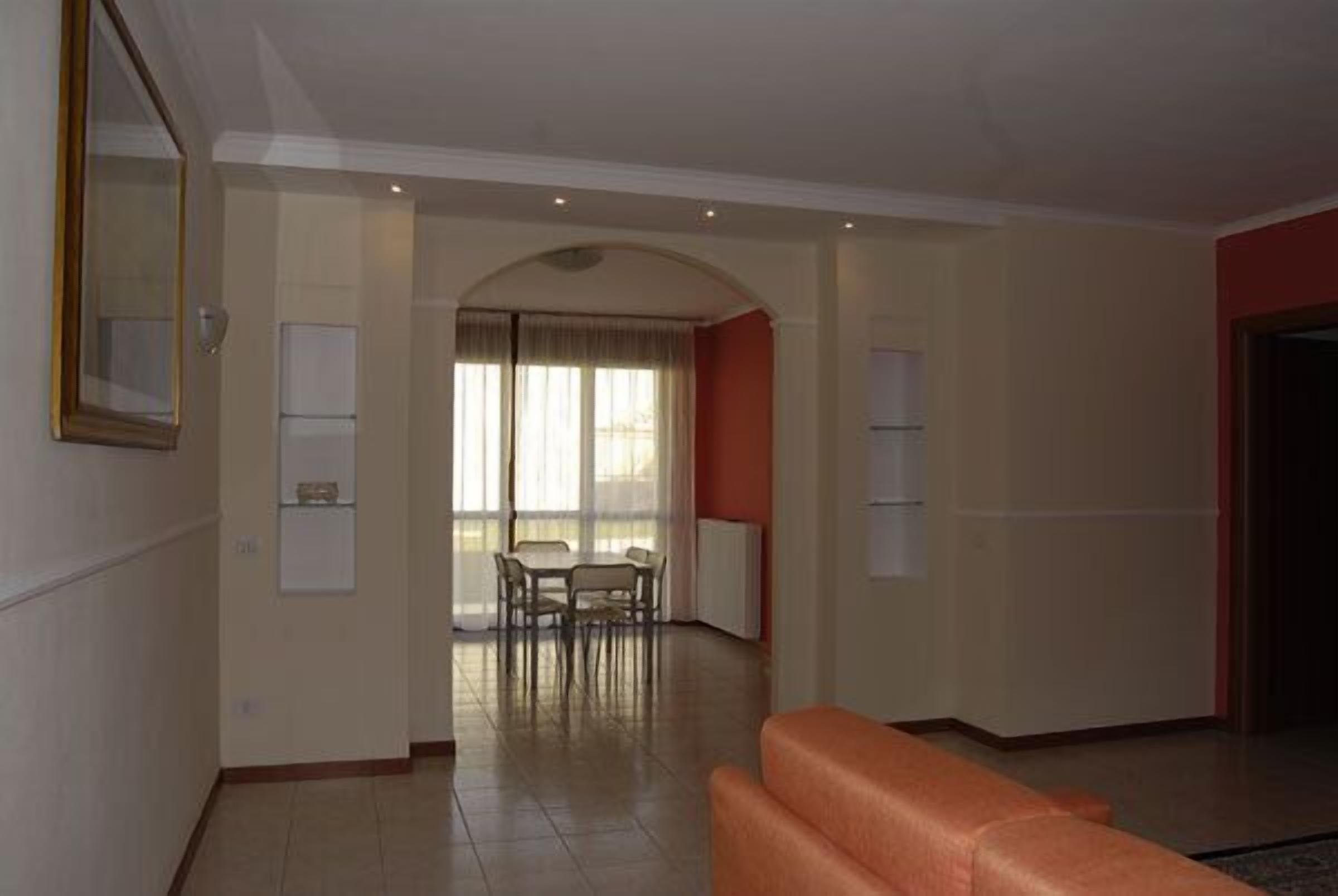 A spacious living area with a sofa, a dining table with chairs, and a large window with curtains.