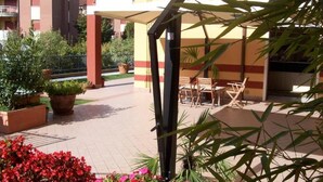 A covered outdoor area with potted plants, a seating area, and a building in the background. - Residence Garda Palace  (Peschiera del Garda)