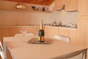 Une cuisine avec des meubles de rangement en bois, un plan de travail blanc et une bouteille de champagne posée sur un plateau.