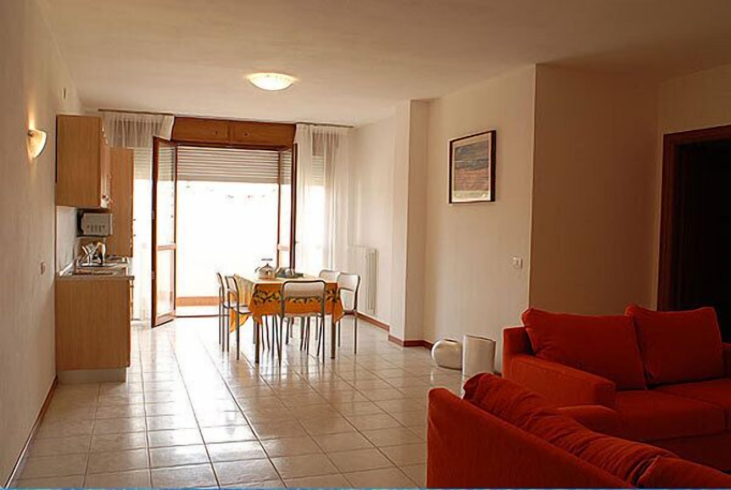Una sala de estar con un sofá rojo, un comedor con mesa y sillas, y una cocina con armarios y encimera.