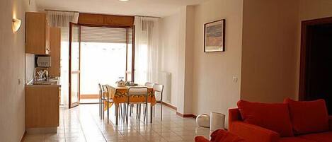Una sala de estar con un sofá rojo, un comedor con mesa y sillas, y una cocina con armarios y encimera.