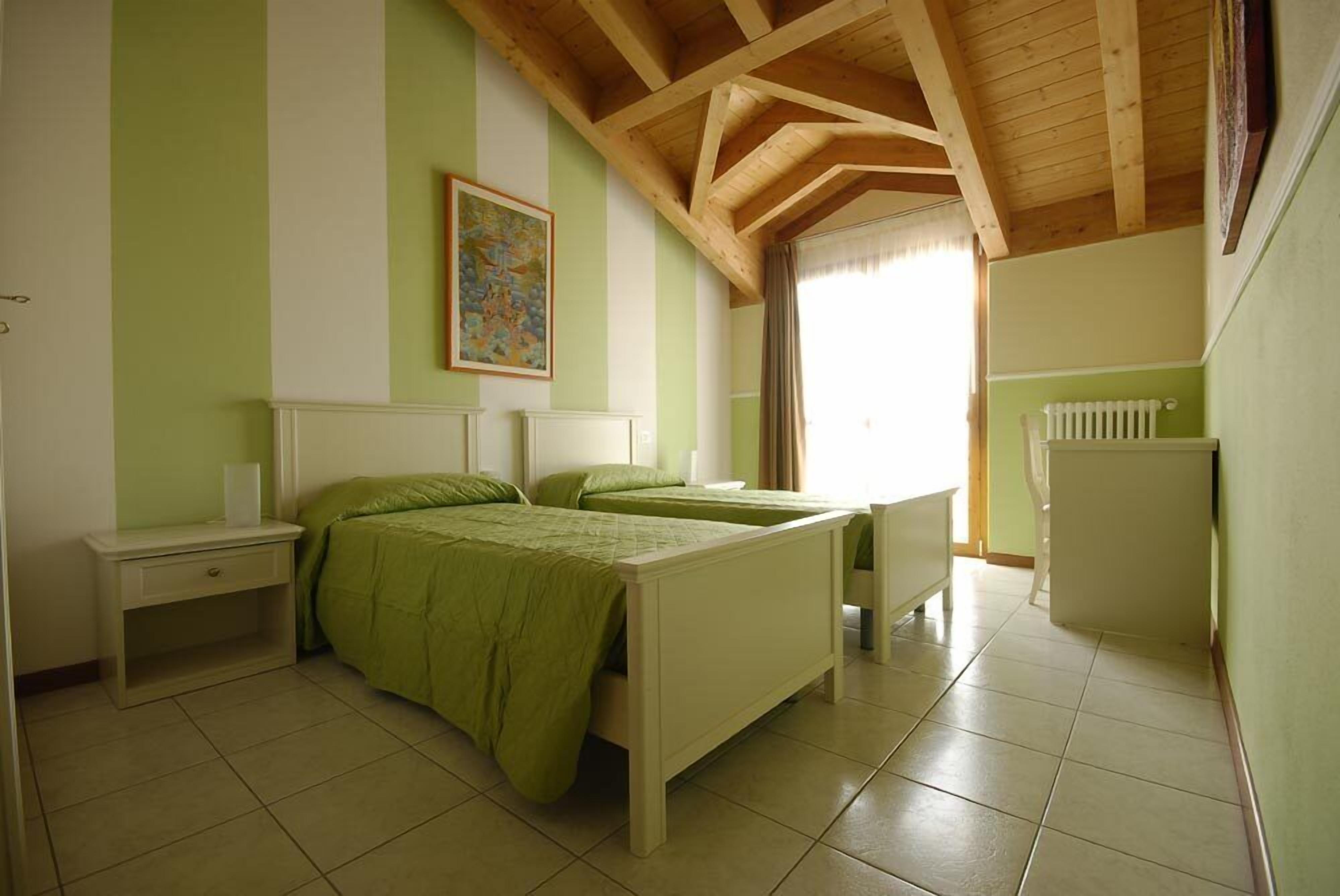 A bedroom with two beds, a nightstand, a dresser, and a radiator.
