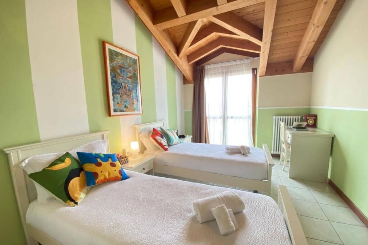 A hotel room with two beds, a painting on the wall, a window with curtains, and a radiator.