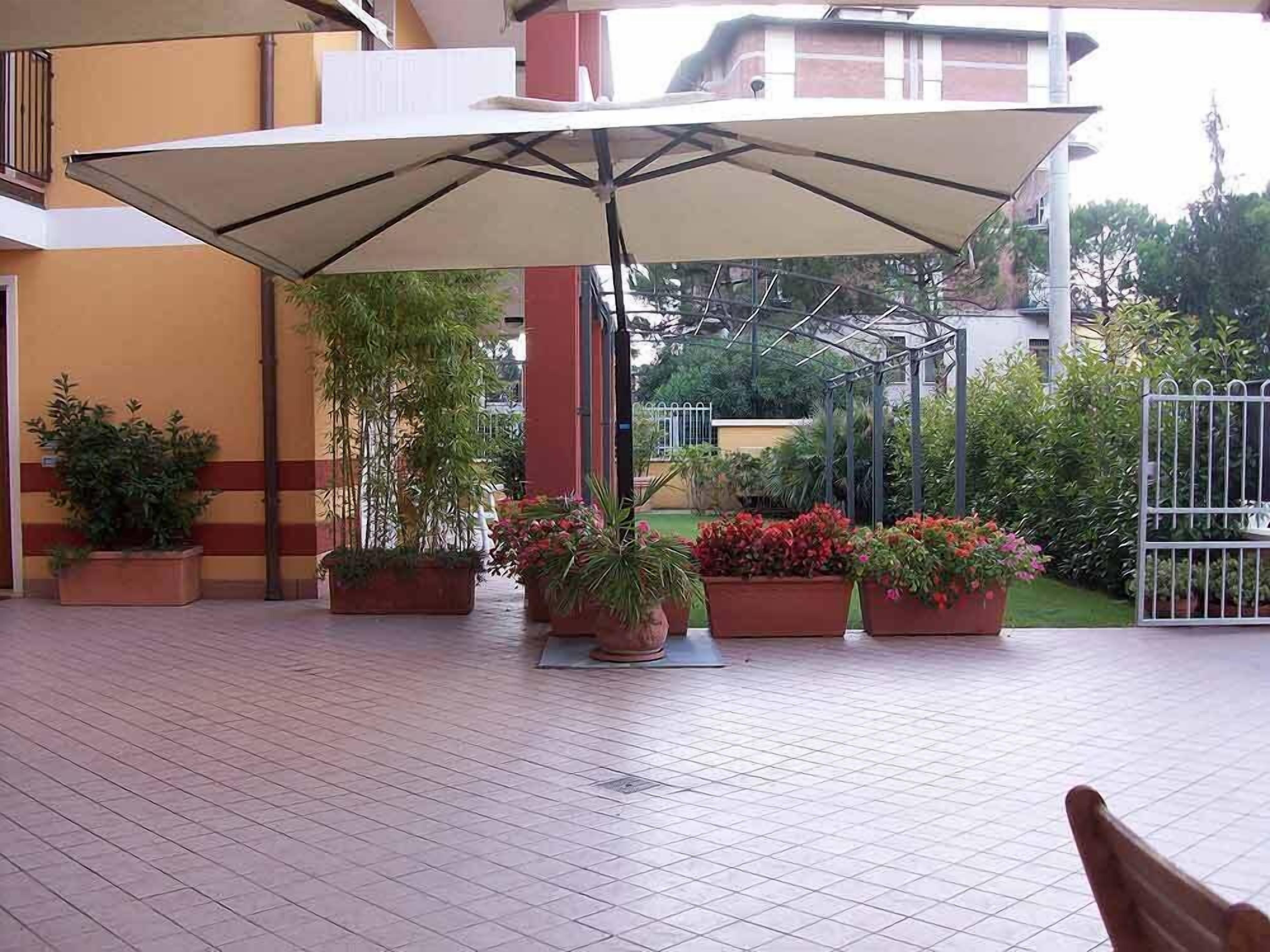 An outdoor patio area with a large umbrella, potted plants, and a tiled floor.