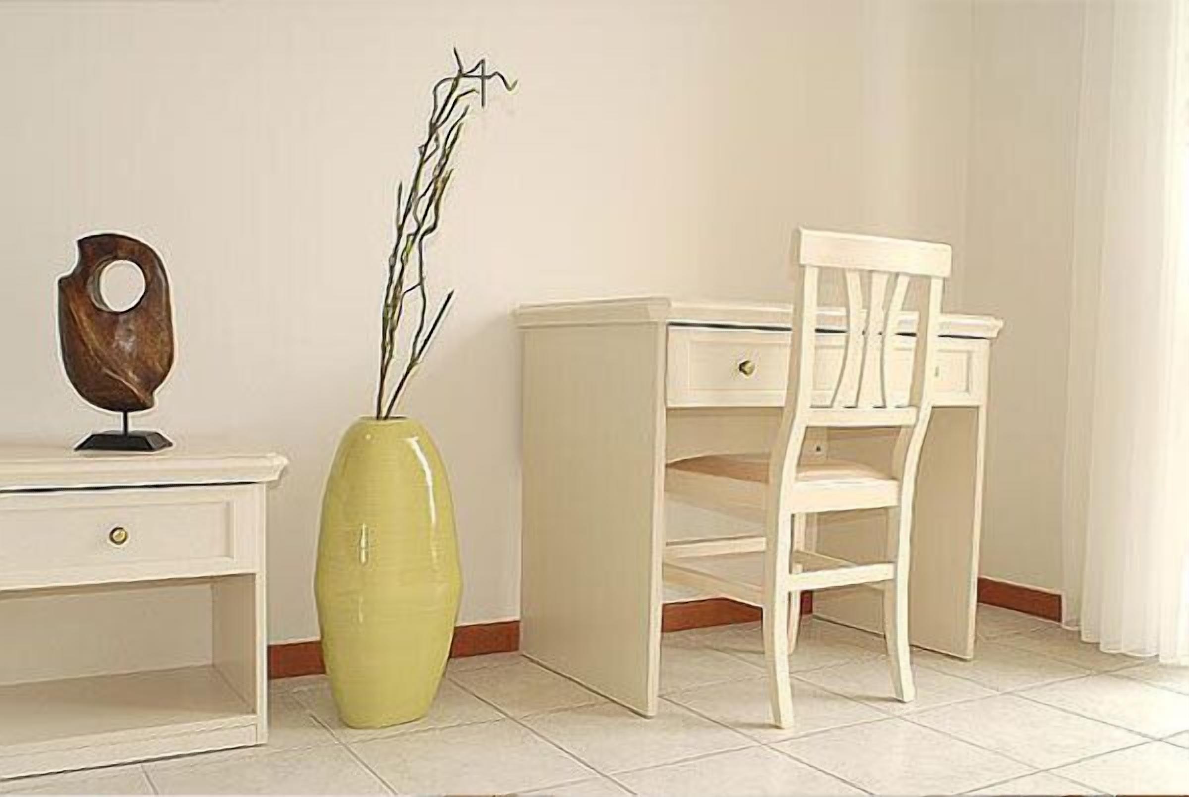 A white desk with a drawer, a white chair, and a yellow vase with a plant.