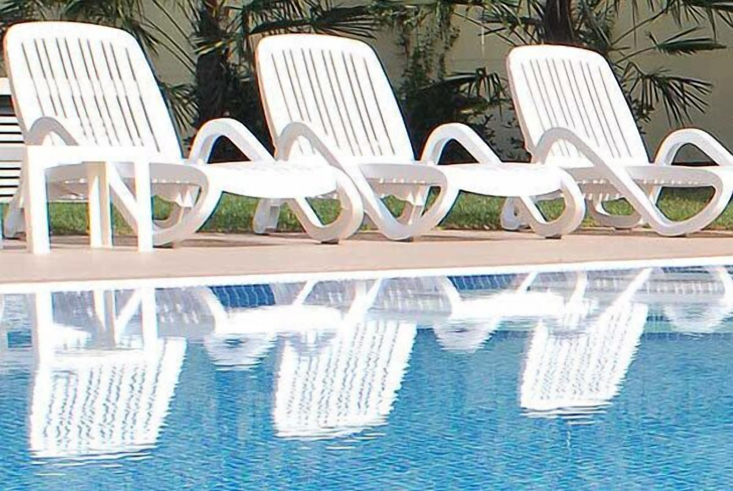 A swimming pool with white lounge chairs arranged in a row.