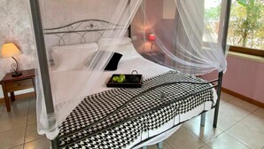 A bed with a black and white checkered bedspread, a bedside table with a lamp, and a window with a view of greenery. - Residence Garda Palace  (Peschiera del Garda)