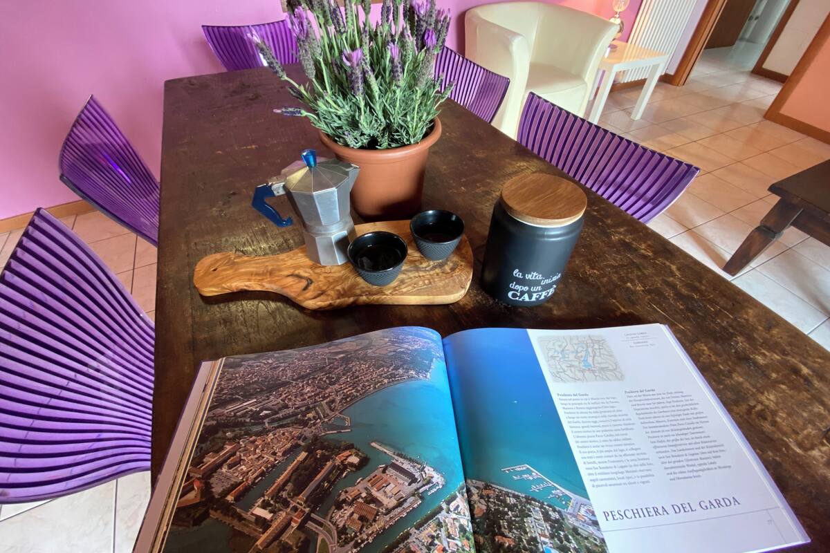 A wooden table with a potted lavender plant, a metal mug, a blue glass, and a book open to a cityscape.