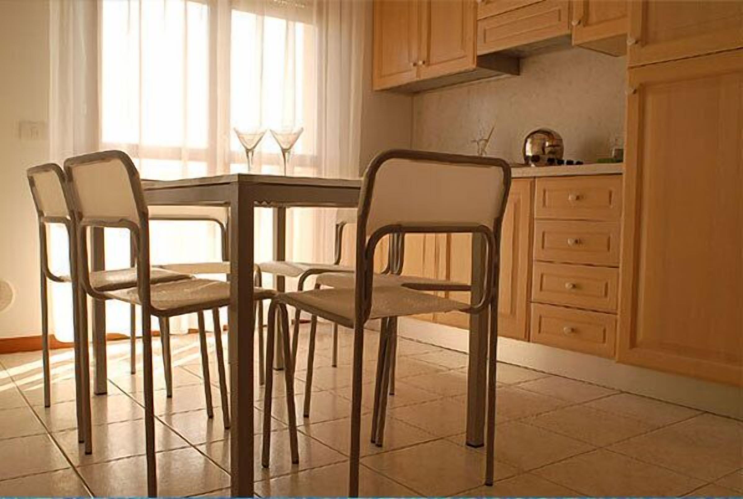 A dining area with a table and four chairs, wooden cabinets, and a window with curtains.