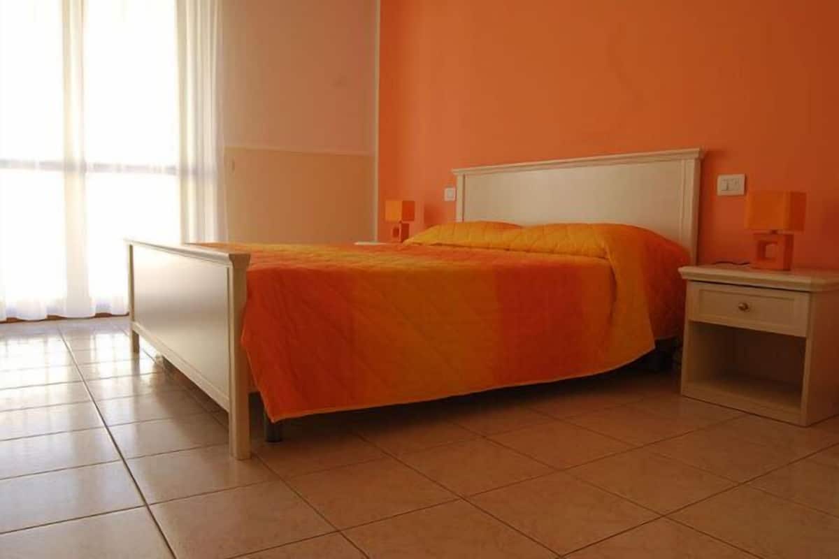 A bed with an orange bedspread, a white headboard, and two bedside lamps on a nightstand.