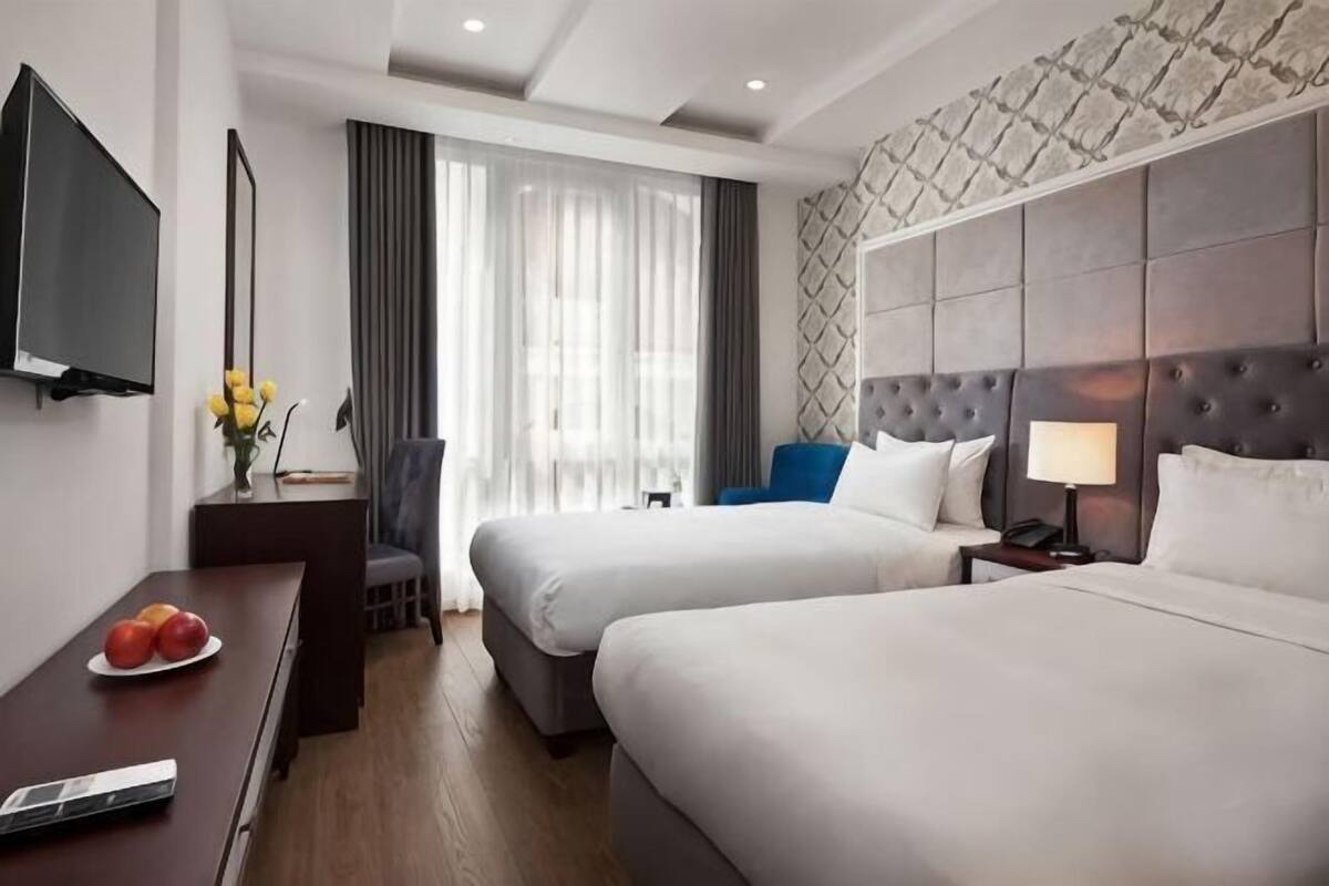 A hotel room with two beds, a desk with a TV, a chair, and a window with curtains.