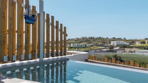A pool with a wooden fence, a clear view of the surrounding landscape, and a distant building. -  Vivere Houses (Milos)