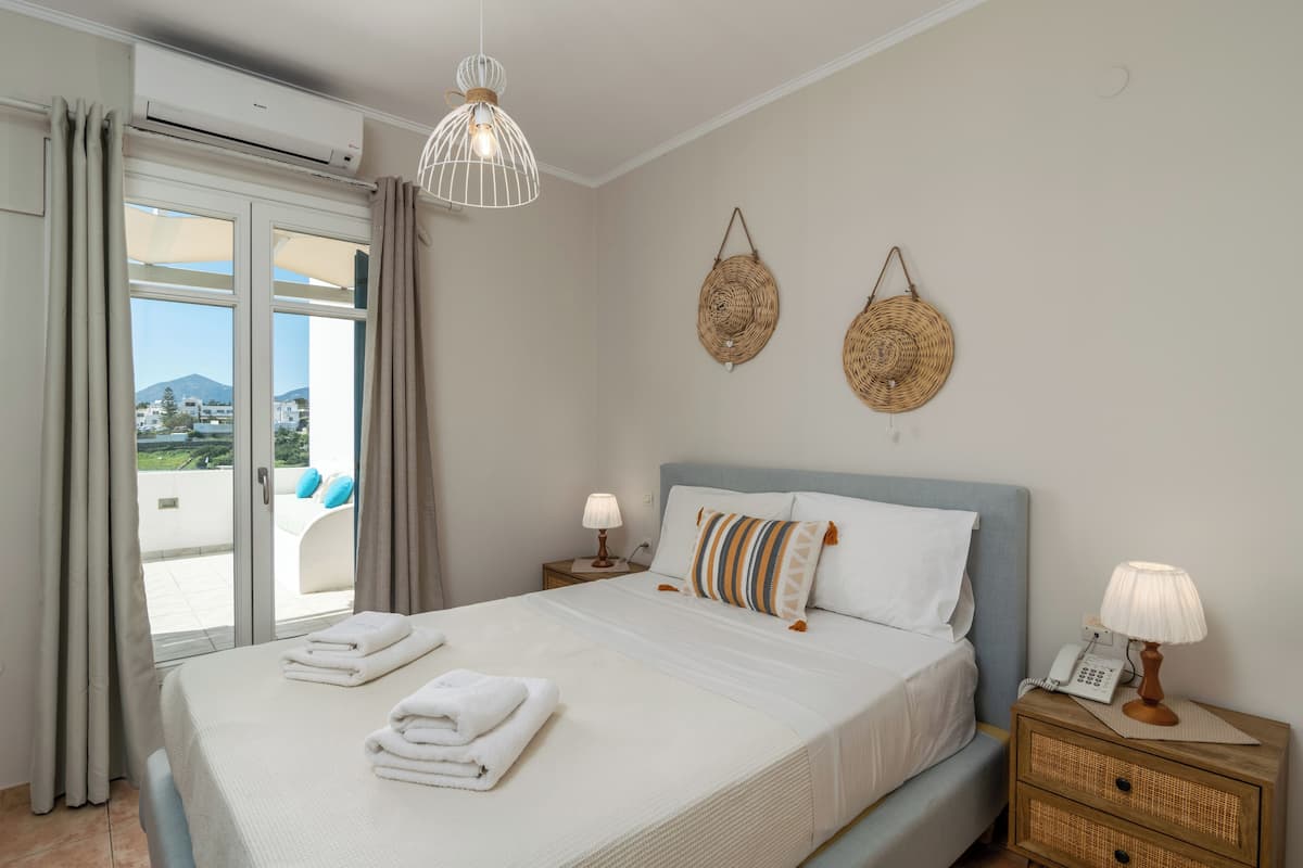 A bedroom with a bed, two bedside tables, a wall-mounted lamp, and a view through a window.